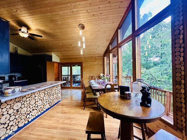 dining space with ceiling fan, wooden ceiling, wood walls, vaulted ceiling, and light wood-type flooring