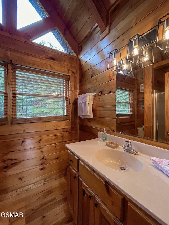 bathroom featuring vanity, vaulted ceiling with skylight, wooden walls, and wood ceiling