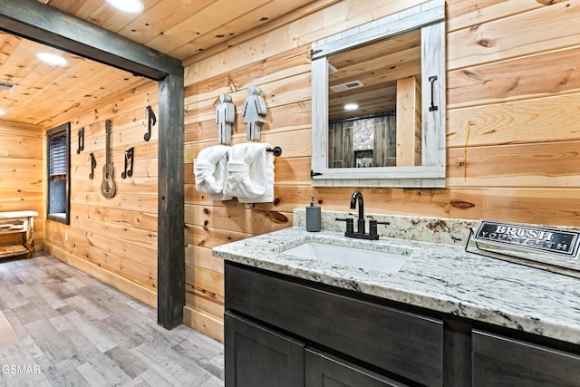 bathroom with wooden walls, vanity, wooden ceiling, wood finished floors, and visible vents