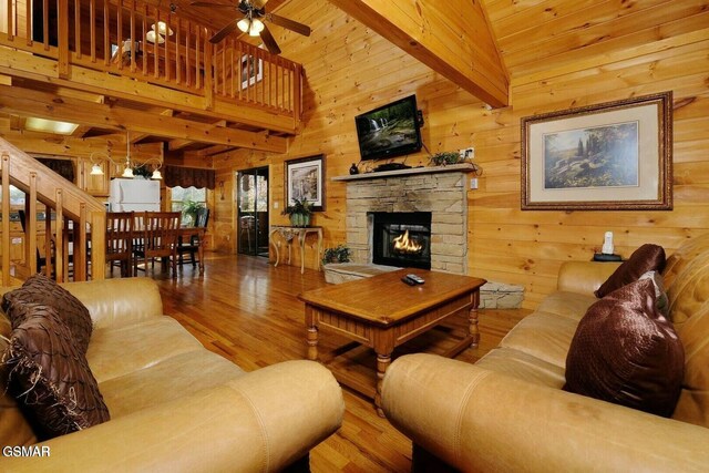 living room featuring ceiling fan, wood-type flooring, beam ceiling, high vaulted ceiling, and a fireplace