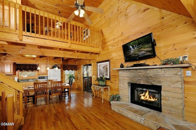 interior space featuring wood walls, high vaulted ceiling, ceiling fan, a fireplace, and wood-type flooring