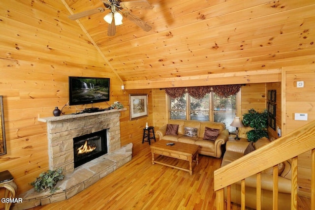 living room with hardwood / wood-style floors, ceiling fan, wood walls, and a stone fireplace