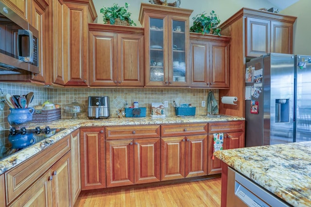 kitchen with decorative backsplash, light wood-type flooring, light stone counters, stainless steel appliances, and sink