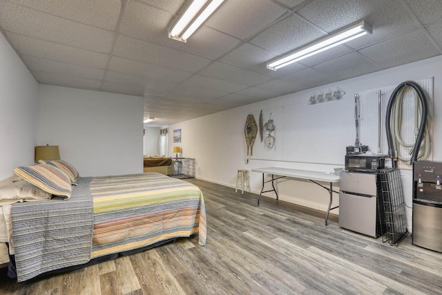 bedroom with hardwood / wood-style floors, a drop ceiling, and stainless steel fridge