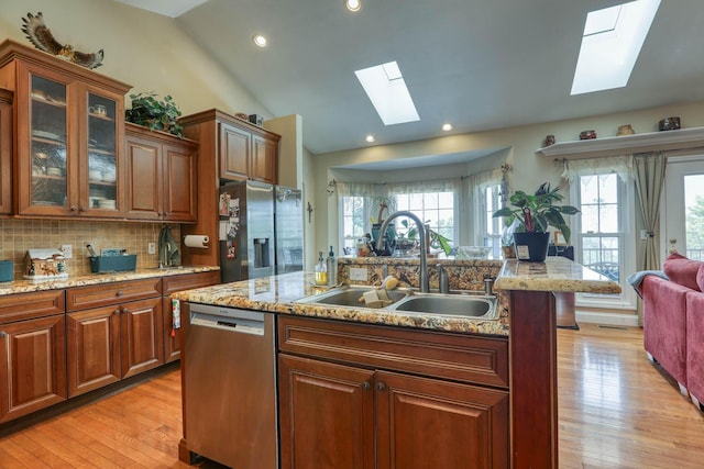 kitchen featuring sink, stainless steel appliances, lofted ceiling with skylight, light hardwood / wood-style floors, and a kitchen island with sink