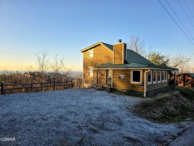 back of house featuring metal roof, driveway, a chimney, and fence