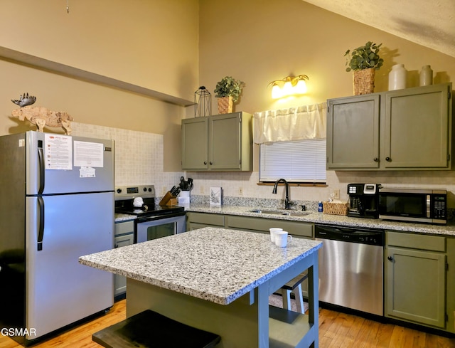 kitchen with light wood finished floors, tasteful backsplash, appliances with stainless steel finishes, a kitchen breakfast bar, and a sink