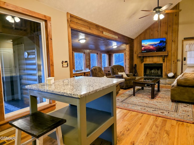 living area with lofted ceiling, ceiling fan, light wood-style floors, wood walls, and a large fireplace