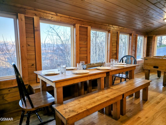 dining area with light wood-style flooring, wood ceiling, and wood walls