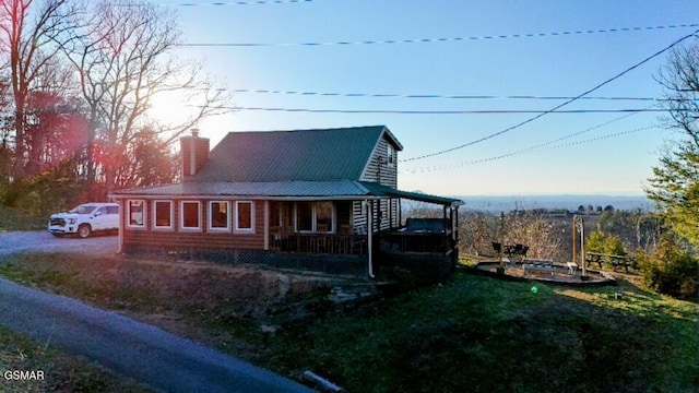 farmhouse-style home featuring covered porch, driveway, a chimney, and metal roof