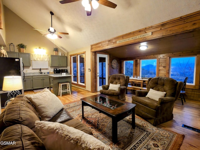 living area with wooden walls, light wood-style flooring, high vaulted ceiling, and a textured ceiling