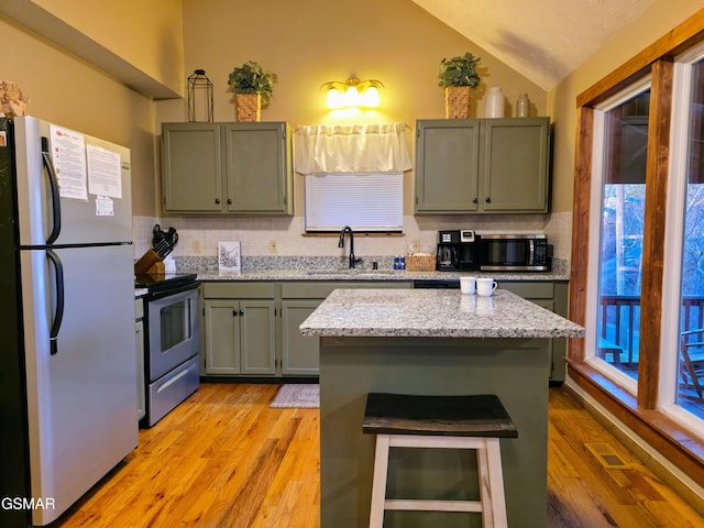 kitchen featuring light wood-type flooring, a sink, tasteful backsplash, appliances with stainless steel finishes, and lofted ceiling