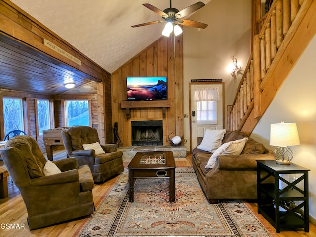 living area featuring stairway, wood walls, a fireplace, wood finished floors, and high vaulted ceiling