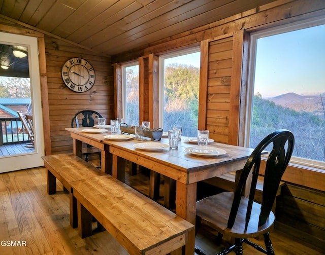 dining space with wood walls, wood ceiling, vaulted ceiling, a mountain view, and wood-type flooring