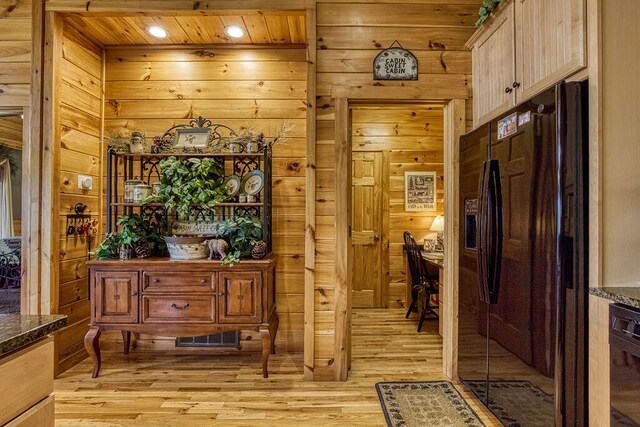 interior space featuring light brown cabinetry, light hardwood / wood-style floors, wooden walls, and black appliances