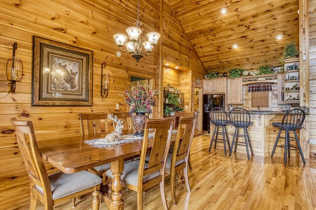 dining space featuring wooden ceiling, high vaulted ceiling, wood walls, a chandelier, and light hardwood / wood-style floors