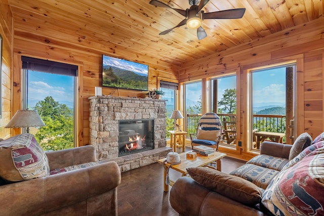 living room with hardwood / wood-style floors, wooden ceiling, a stone fireplace, wooden walls, and ceiling fan