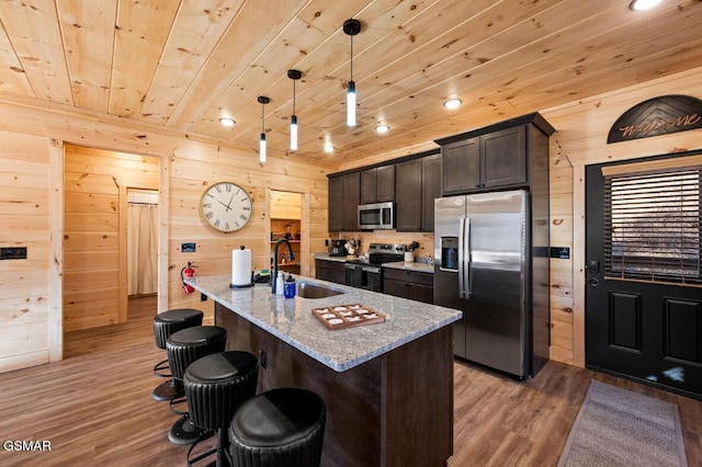 kitchen featuring pendant lighting, sink, stainless steel appliances, light stone countertops, and a center island with sink