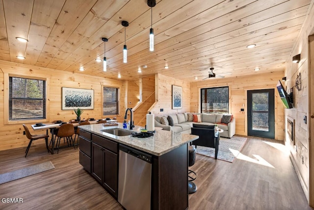 kitchen with light stone counters, decorative light fixtures, a sink, stainless steel dishwasher, and a center island with sink