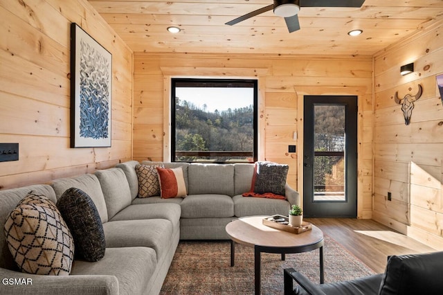 living area with wooden ceiling, wood walls, ceiling fan, and wood finished floors