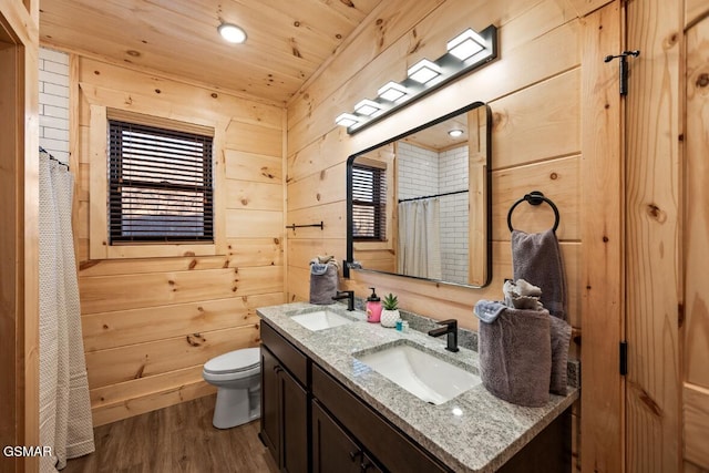 full bathroom with double vanity, wood finished floors, a sink, and wooden walls