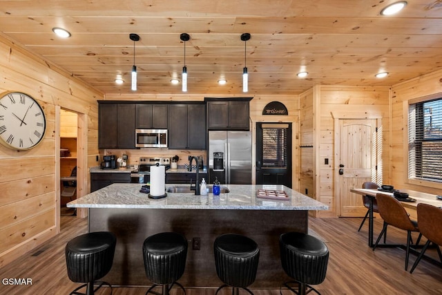 kitchen featuring appliances with stainless steel finishes, a center island with sink, and decorative light fixtures