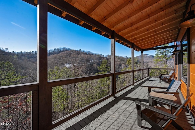 sunroom / solarium with lofted ceiling with beams, wooden ceiling, a mountain view, and a wooded view