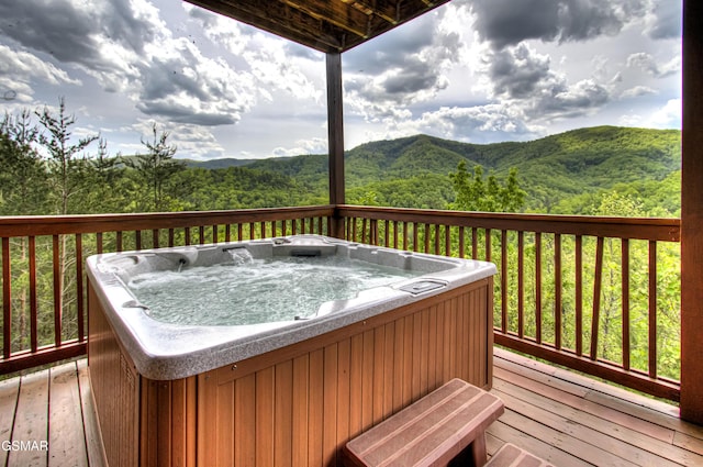 wooden deck featuring a mountain view, a hot tub, and a wooded view