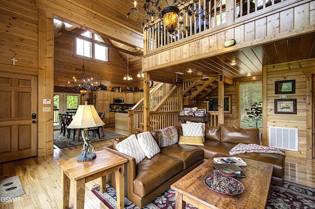 living room with an inviting chandelier, wood walls, visible vents, high vaulted ceiling, and stairway