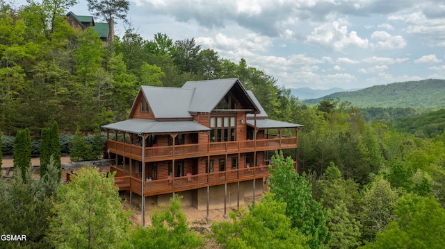 rear view of property with a deck with mountain view, a wooded view, and metal roof