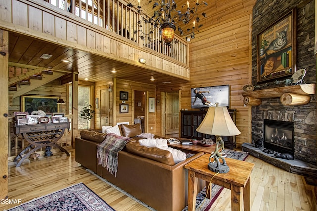 living area with wood-type flooring, wood walls, a stone fireplace, and a towering ceiling