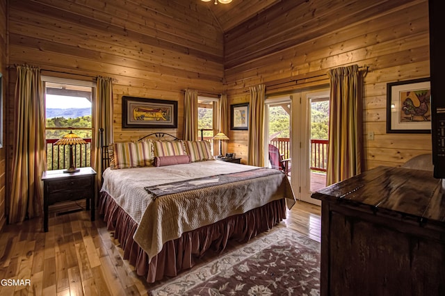 bedroom with access to outside, light wood finished floors, and wood walls