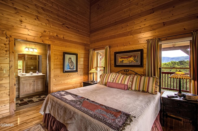 bedroom featuring wooden walls, wood finished floors, and ensuite bath