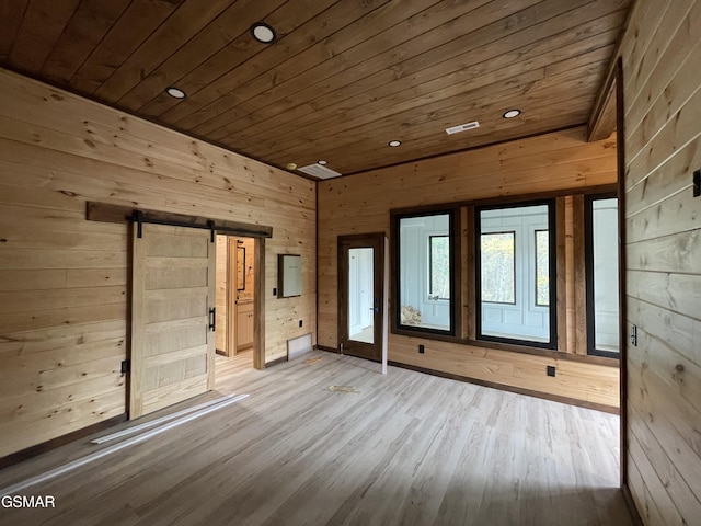 unfurnished room featuring a barn door, wooden walls, and wood ceiling