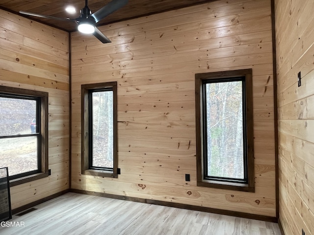 empty room with wood walls, ceiling fan, and light hardwood / wood-style floors