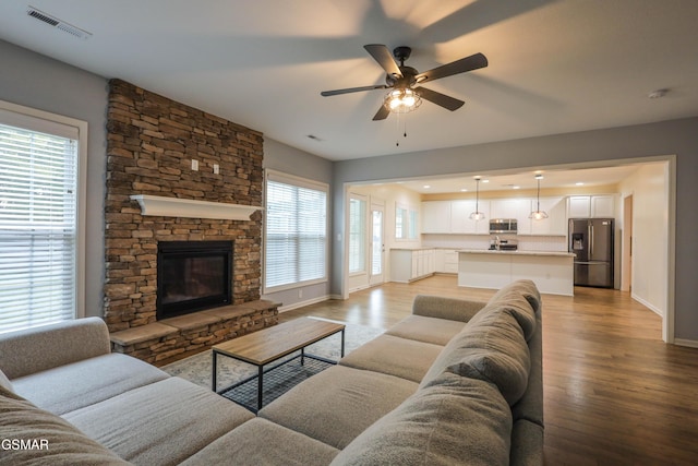 living area featuring light wood-type flooring, visible vents, baseboards, and a stone fireplace