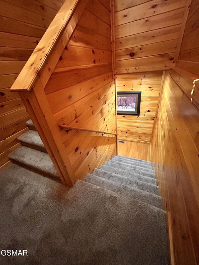 stairway featuring wood walls, wooden ceiling, and carpet floors