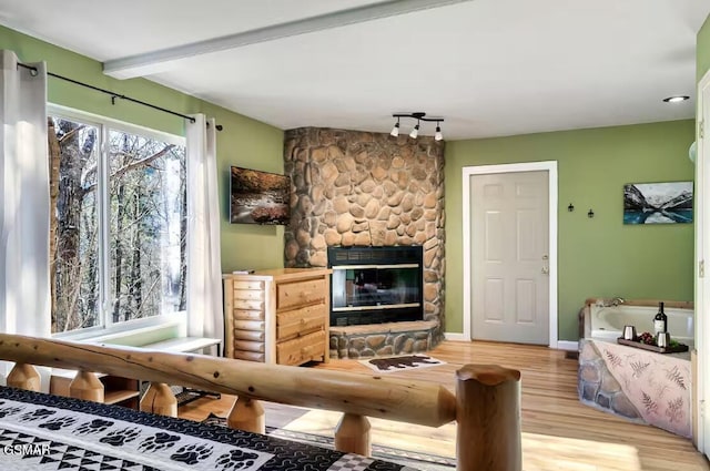 living room with beamed ceiling, a stone fireplace, and wood-type flooring