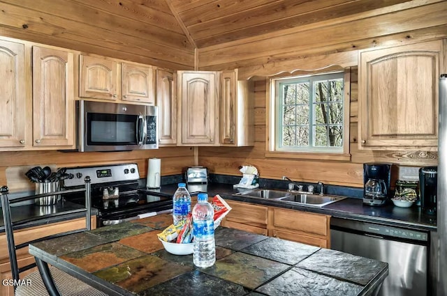 kitchen featuring appliances with stainless steel finishes, light brown cabinetry, sink, lofted ceiling, and wood walls