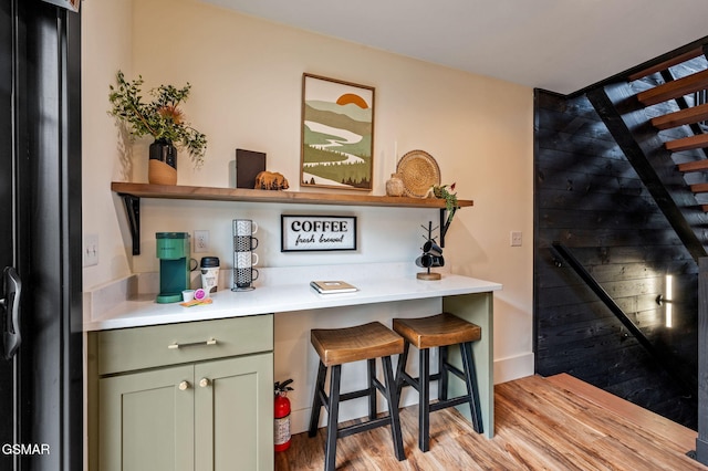 bar with light wood finished floors, black refrigerator with ice dispenser, and stairs