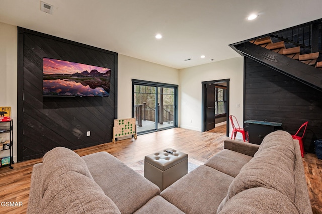 living area with an accent wall, visible vents, wood walls, and light wood finished floors