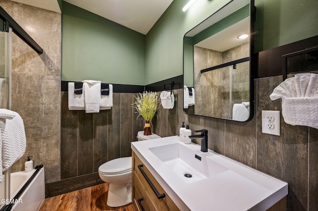 full bathroom featuring toilet, wood finished floors, vanity, tiled shower, and wainscoting