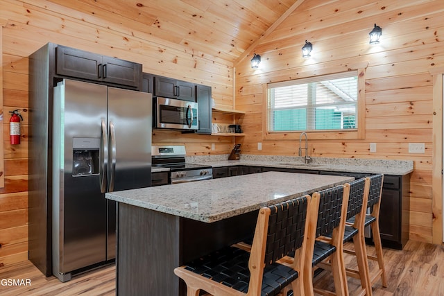 1012 Pinyon Cir, Pigeon Forge, TN 37863 - kitchen featuring appliances with stainless steel finishes, a breakfast bar, wood walls, light wood-type flooring, and light stone counters