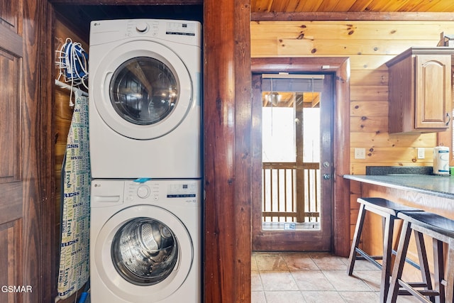 laundry room featuring light tile patterned floors, wooden walls, and stacked washer and clothes dryer