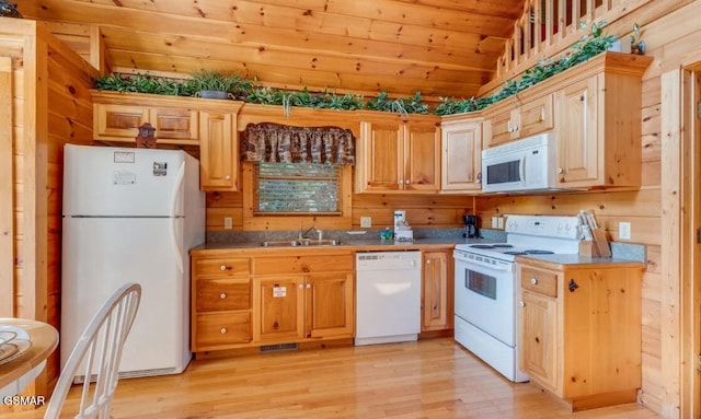 kitchen with sink, white appliances, light hardwood / wood-style floors, wooden walls, and lofted ceiling