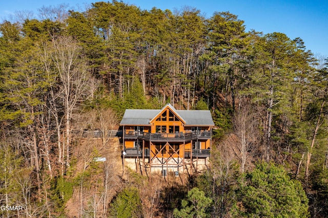 back of house featuring metal roof, a balcony, and a forest view