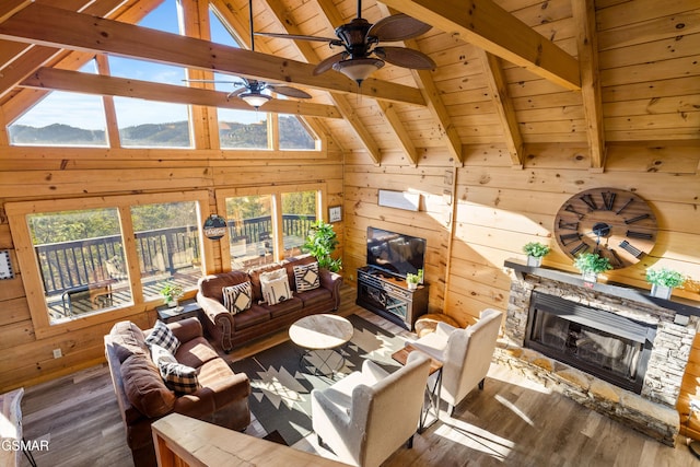 living area with wood ceiling, wood finished floors, a stone fireplace, wood walls, and beam ceiling