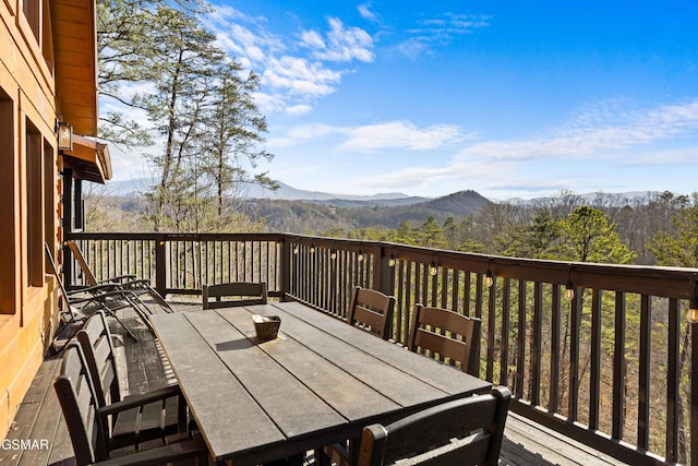 wooden terrace with a forest view, a mountain view, and outdoor dining area