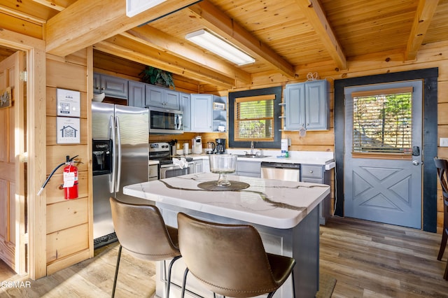 kitchen with wooden walls, beam ceiling, stainless steel appliances, light wood-type flooring, and a sink