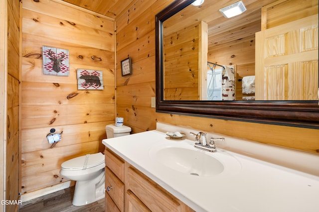 bathroom featuring wood finished floors, wood walls, vanity, and toilet